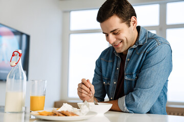 Fototapeta na wymiar Happy handsome young man smiling while having breakfast at home