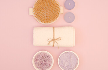 Fototapeta na wymiar The concept of spa care, relaxation, care and beauty about your body. A set of skin care products. Massage brush, sea salt, scrub, tea candles and a towel on a pink background. Top view, flat lay
