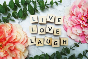 Live LoveLaught alphabet letter with green leave and pink flower flat lay on marble background