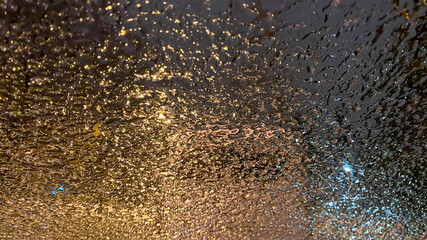 Frozen ice in the bright glow of the light on the car window at night or in the evening out of focus. Drops on glass. Aspect bokeh texture. Winter