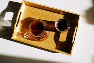Freshly brewed black filter coffee is served on a bamboo tray on sunlit white table. Top view