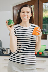 Woman in the kitchen is smiling and holding peppers in her hands. Food blogger in the kitchen. To eat healthy food. Cooking with joy. White kitchen at home