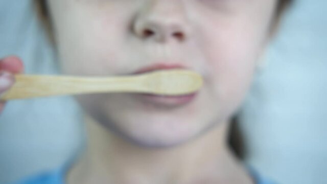 Teeth brush made of wood. A child hold a teethbrush made of wood and brush her teeth with organic paste in the bathroom.