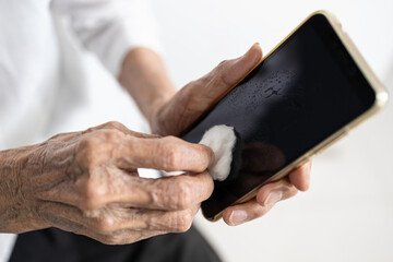 Hands of old elderly using cotton wool with alcohol to wipe the phone screen,cleaning smart phone,stop spreading Coronavirus,COVID-19 outbreak,concept of wipe clean surface that are frequently touched