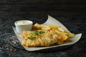 Baking paper with fried fish and chips on black smokey table