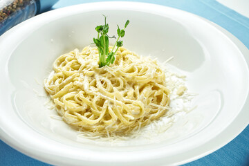 Classic, homemade Italian pasta (spaghetti) in cheese sauce with parmesan and Dorblu white plate on a blue tablecloth. Close up view.