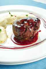 Fillet mignon steak medium rare with berry sauce and potato gnocchi in a white plate on a blue tablecloth