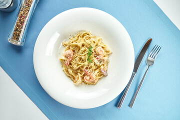 Classic, homemade Italian pasta (spaghetti) in cheese sauce with with shrimps and seafood in a white plate on a blue tablecloth