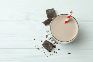 Glass of chocolate milkshake and chocolate pieces on white wooden table