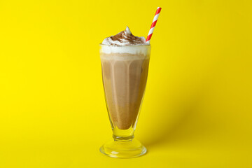 Glass of chocolate milkshake with straw on yellow background