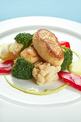 Diet turkey cutlets garnished with steamed vegetables in a white plate on a blue tablecloth.