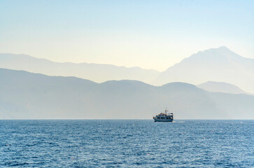 Summer concept: Sea and mountain view on a misty day. A single boat floating on the water. Blue degradation with copy space