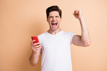 Portrait of delighted guy closed eyes open mouth scream yeah fist up isolated on beige color background