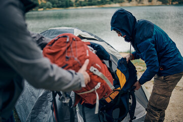 Two men on a camping trip in the nature putting backpack in a tent.