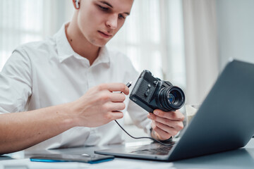 Professional photographer with tattooed arm looks at photocamera he holding it. Hipster guy wearing formal clothing working in office.