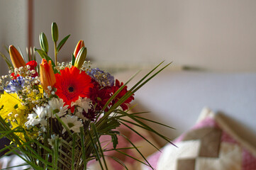 Colorful flower bouquet in vase on glass table and sofa in background. Spring decoration in a house