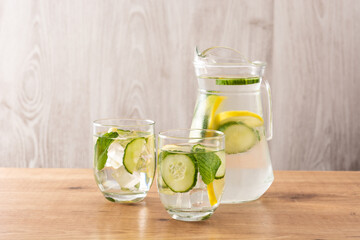 Sassy water or water with cucumber and lemon on wooden table	