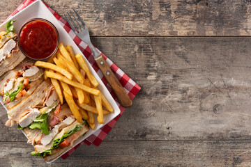 Club sandwich and French fries with ketchup sauce on wooden table. Copy space