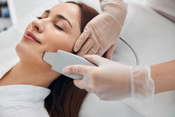 Smiling woman receiving facial treatment in cosmetology clinic