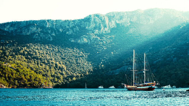 Summer concept: A Turkish gullet yacht anchored at the Aegean sea with sun beam in background. Natural photo with copy space. Green and blue contrast