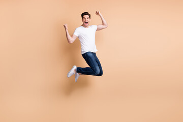 Fototapeta na wymiar Full size profile photo of hooray brunet man jump yell wear t-shirt jeans sneakers isolated on beige background