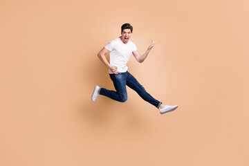 Fototapeta na wymiar Full size profile photo of hooray brunet man jump play guitar yell wear t-shirt jeans sneakers isolated on beige color background