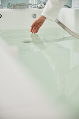 Female hand checking water in bathtub before spa procedure