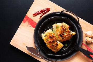 Food concept spot focus homemade butter, garlic, bread crumbs and cheese crunchy Baked cod fish in skillet iron cast pan on black background with copy space