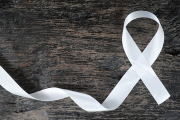 Top view of white ribbon on dark wood background. Lung cancer awareness concept.	