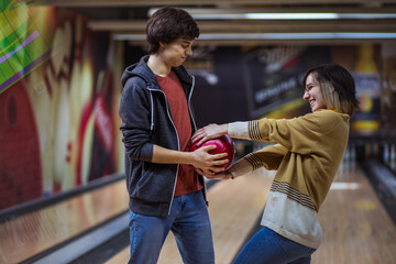 Young couple standing in a bowling alley and fighting for a ball.