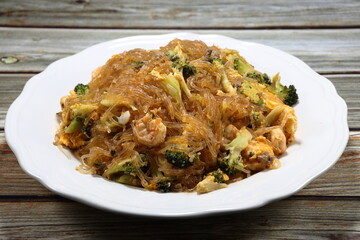 Traditional fried instant vermicelli or glass noodle mixed with fresh peeled shrimp, chopped broccoli, chilly and egg serving on the plate. Famous spicy Korea noodle menu in Asia restaurant. 