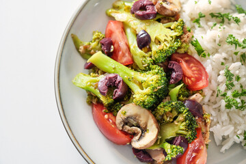 Oven vegetables of broccoli, mushrooms, tomatoes and olives with rice and parsley garnish, healthy cooking with fresh ingredients, close up from above, selected focus