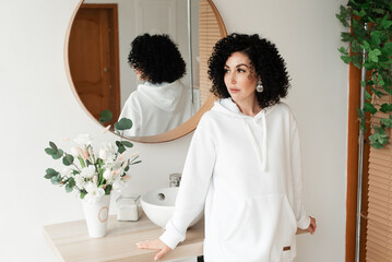 A woman with African curls in stands against the background of a mirror and looks to the side