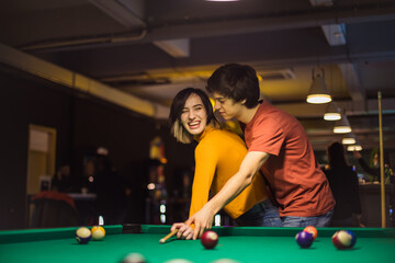 Young couple spending time in billiard room. Boyfriend teaching his girlfriend to playing billiard.