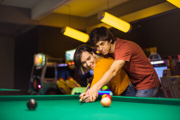 Young couple spending time in billiard room. Boyfriend teaching his girlfriend to playing billiard.