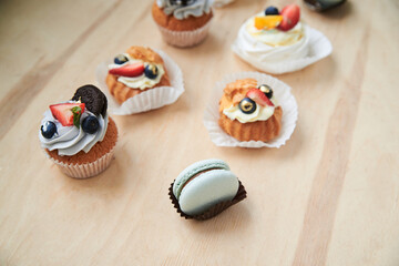 Baked cupcakes with cream cheese icing and fruits on top, mint macarons. Colorful sweet pastries on wooden table buffet. Festive holiday celebration. party. Fancy mini desserts.
