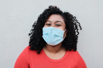 Young african woman smiling on camera while wearing safety mask during coronavirus outbreak - Focus on face