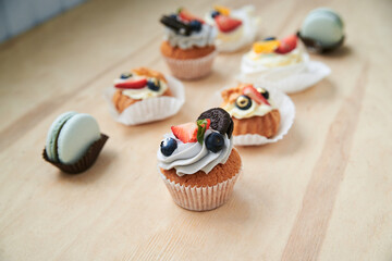Baked cupcakes with cream cheese icing and fruits on top, mint macarons. Colorful sweet pastries on wooden table buffet. Festive holiday celebration. party. Fancy mini desserts.
