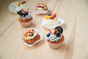 Baked cupcakes with cream cheese icing and fruits on top, mint macarons. Colorful sweet pastries on wooden table buffet. Festive holiday celebration. party. Fancy mini desserts.