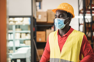 African man working inside warehouse while wearing safety mask during coronavirus outbreak - Focus on face