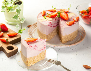 Festive raw vegan strawberry cake decorated with berries and almond petals, gluten, egg and sugar free, shot from a high angle. Slice of cake served on a glass plate. Healthy food concept