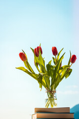 bunch of tulips in a glass vase against blue sky, colorful spring flowers on blurred background with free copy space, springtime concept