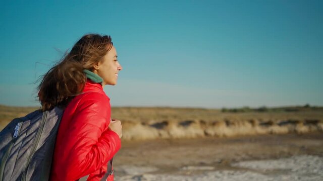 slow motion portrait of happy confident and joyful young woman hiker in red jacket walking on salty lake coast with clay shore