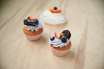 Three baked cupcakes with cream cheese icing, strawberry, blueberry and oreo on top. Colorful sweet pastries on wooden table buffet. Festive holiday celebration. party. Fancy mini desserts.