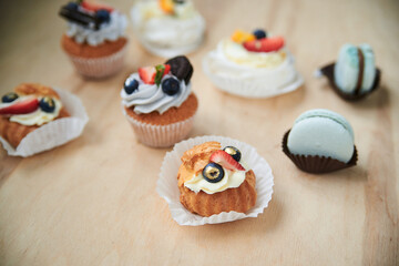 Baked cupcakes with cream cheese icing and fruits on top, mint macarons. Colorful sweet pastries on wooden table buffet. Festive holiday celebration. party. Fancy mini desserts.