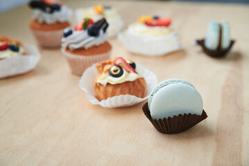 Baked cupcakes with cream cheese icing and fruits on top, mint macarons. Colorful sweet pastries on wooden table buffet. Festive holiday celebration. party. Fancy mini desserts.