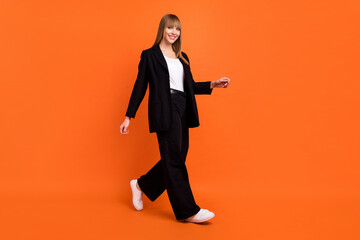 Full length body size view of attractive cheerful girl walking strolling office look isolated over bright orange color background