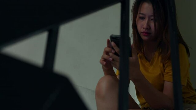 4K Depressed Asian woman sitting on stairs using mobile phone with unhappy and boredom. Loneliness sad female being alone with stressed and negative emotion. Mental health and life problem concept.