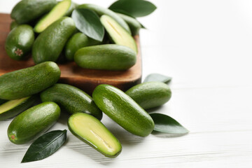 Fresh seedless avocados with green leaves on white wooden table, closeup. Space for text
