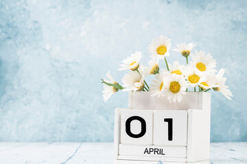 White cube calendar for april decorated with daisy flowers over blue with copy space